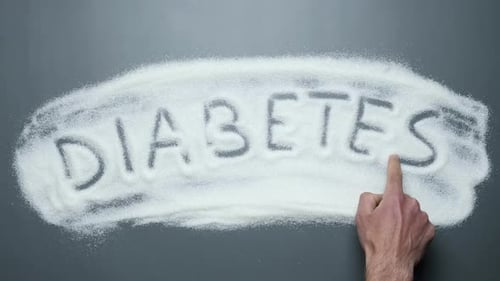 Hand Writes Diabetes in Sugar Pile on Gray Surface