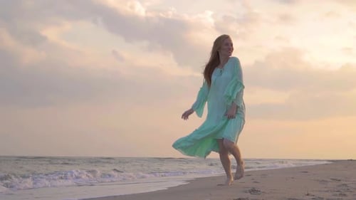 Das junge rothaarige lächelnde Mädchen läuft im Sommer im grünen Kleid am Strand am Meer