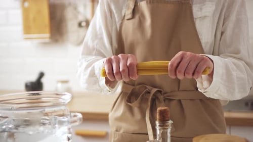 Woman Breaking Spaghetti in Bright Kitchen