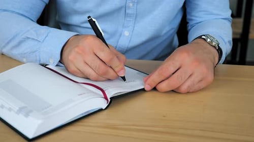 Close up businessman sitting on chair at table works at home office writes information notebook