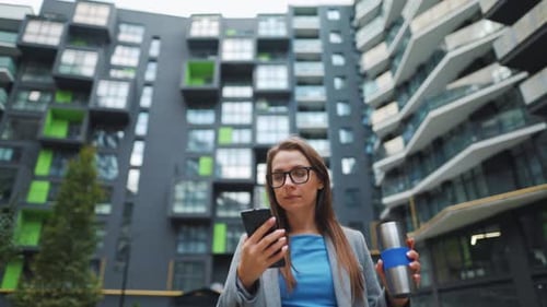 Formally Dressed Woman Walking Down the Street in a Business District with Thermo Cup in Hand and