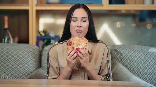 Woman Eating Bagel In Cafe Setting