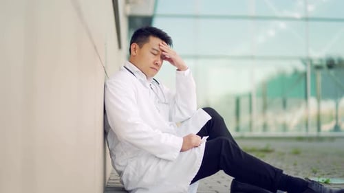 portrait stressful Asian doctor sitting or standing outside a hospital