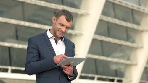 Smiling Man Using Tablet Outside Office Building