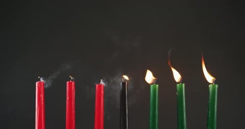 Composition of halloween green, black and red lit candles being blown off against black background