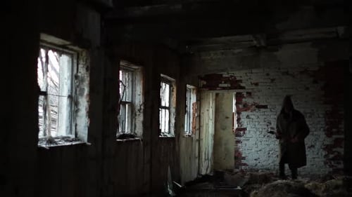 Silhouette of Man in Dark Cloak Walking Through Abandoned Building with an Ax