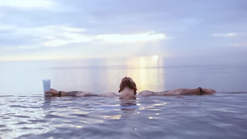 Modelo masculino descansando su cabeza en el borde de la piscina infinita