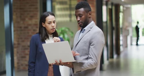 Two happy diverse business people working together, using laptop in modern office