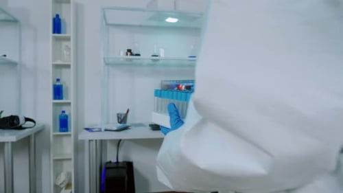 Químico en traje de protección lleva tubos de ensayo en laboratorio estéril