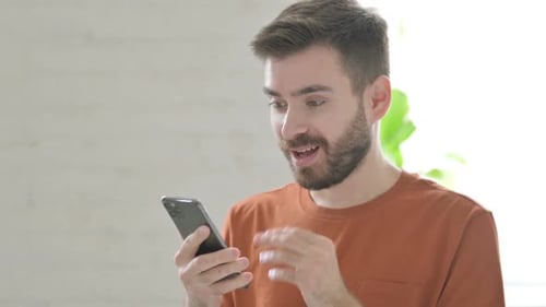 Man Celebrates Looking at Smartphone in Brightly Lit Home