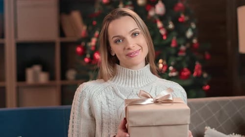 Woman Holding Christmas Gift Near Decorated Tree
