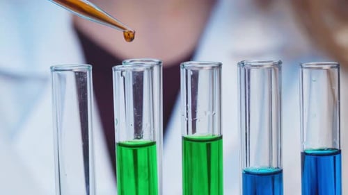 Close Up of Pipette Dropping Samples of Color Liquid Into Test Tubes in Laboratory