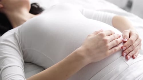 Pregnant Woman Lying in Bed Touching Stomach