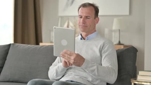 Man Sitting on Couch Using Tablet