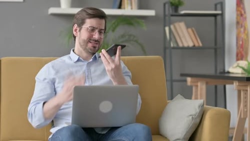 Man Talking on Smartphone With Laptop at Home