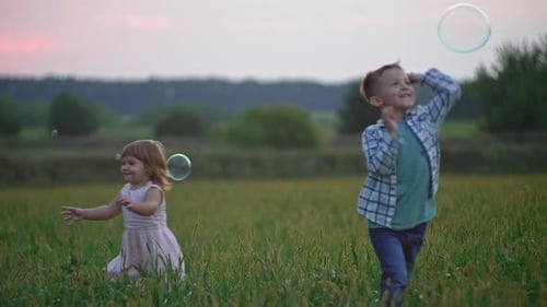 Children Play with Bubbles in Grassy Field at Sunset