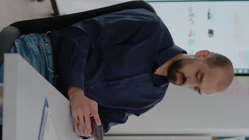 Man With Beard Sitting at Desk Looking at Phone