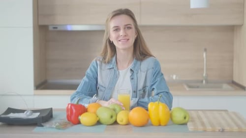 Smiling Woman Drinks Juice Among Fruits and Vegetables