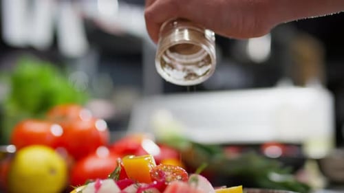 Seasoning a fresh colorful salad in the kitchen
