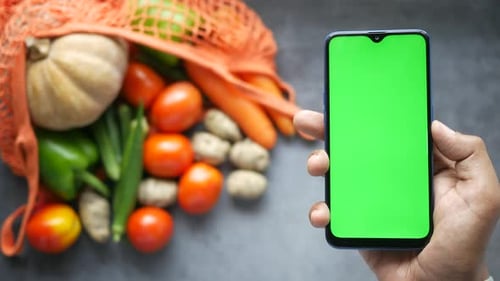 Top View of Man's Hand Holding Smart Phone with Fresh Vegetable on Table