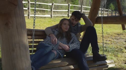 Young Couple Cuddling Together on a Wooden Swing
