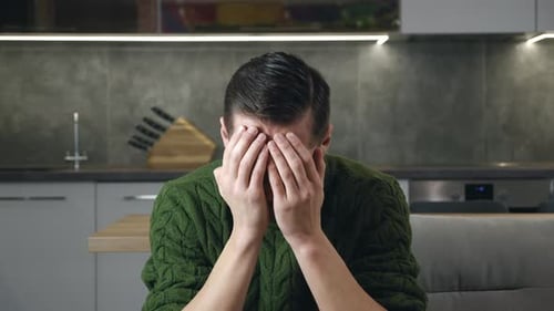 Man Covering Face with Hands in Kitchen