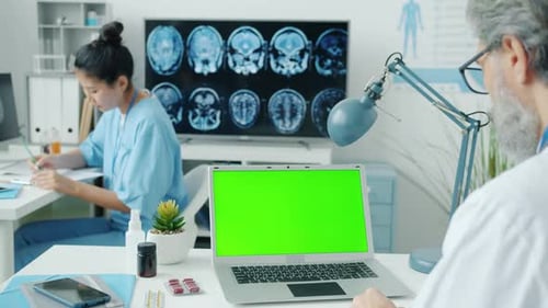 Doctor Using Chroma Key Green Screen Laptop While Nurse Writing Medical Records in Hospital