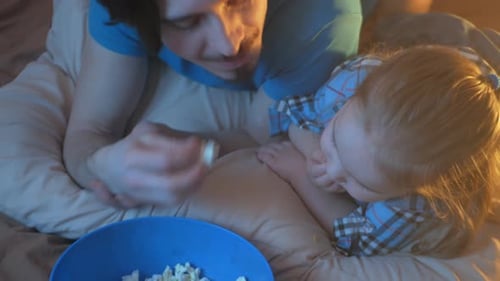 Father and Child Eating Popcorn on Bed