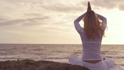 Silhouette young woman practicing yoga on the beach at sunset