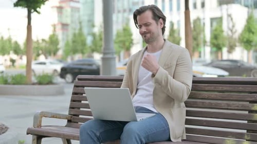 Man With Wrist Pain Works on Laptop Outdoors