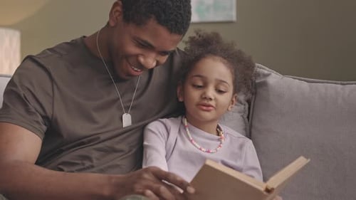 Loving Father Reads Story to Young Daughter on Couch