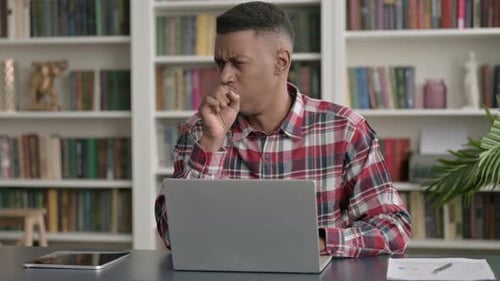 African Man Coughing while using Laptop in Office