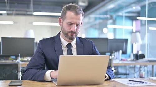 Thoughtful Businessman Works on Laptop in Office