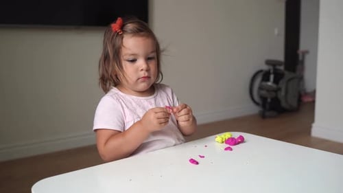 Little Girl Plays with Modeling Clay at Table