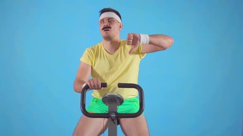 Man Exercising on Bike Giving Thumbs Down in Studio