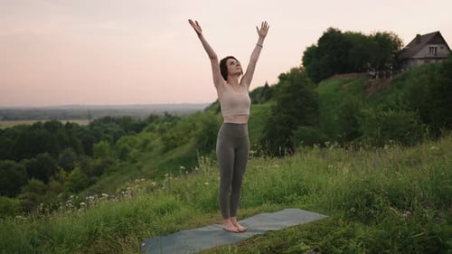 Woman Practices Yoga on Hillside at Sunset