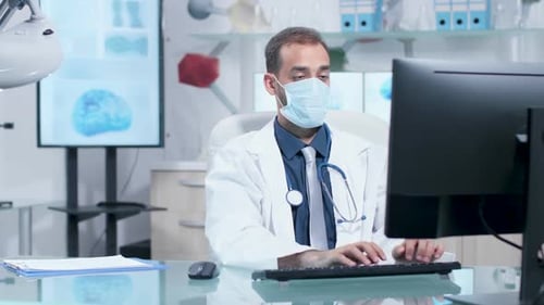 Jeune médecin portant un masque tapant à l'ordinateur