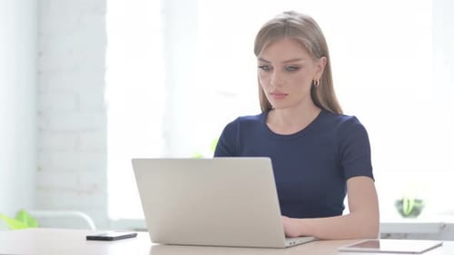 Woman Smiles at Camera While Typing on Laptop