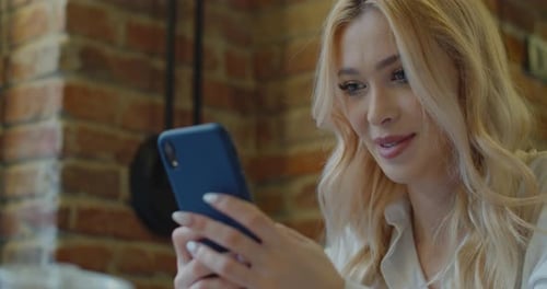 Beautiful Woman Sitting at a Cafe Using Mobile Phone and Smiling