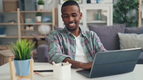 Erfolgreicher afroamerikanischer Freelancer arbeitet zu Hause mit Laptop am Schreibtisch im Studio