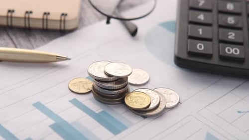 Stack of Coins Financial Graph Calculator and Notepad on Table
