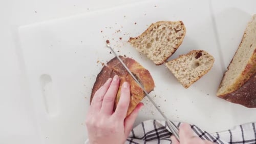 Flache Lage. Frisch gebackenes Sauerteig-Weizenbrot auf einem weißen Schneidebrett schneiden.