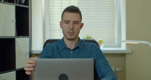 Young Adult Opens Laptop at His Desk