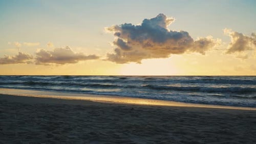 Sonnenuntergang hinter Wolken über Meereswellen und Sandstrand