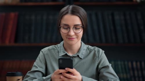 Brunette Female Student Chatting Smartphone Texting Message Studying at Library Enjoy Break