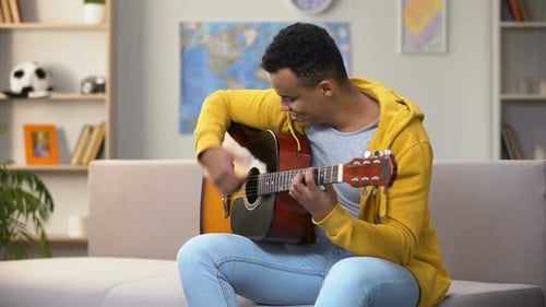 Young Man Playing Guitar on Couch Indoors