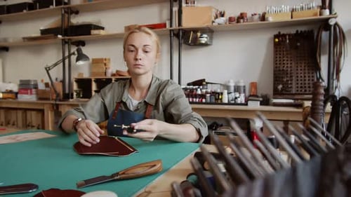 Woman Crafts Leather Item at Workbench in Workshop