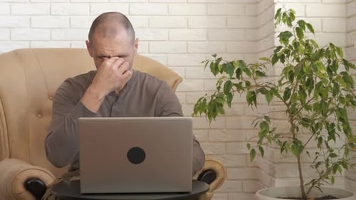 Man Using Laptop at Home Rubs Tired Eyes