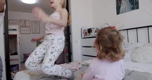 Sisters Playfully Jump on Bed at Home