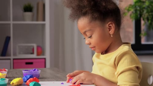 Little Girl Playing with Colorful Plasticine at Table